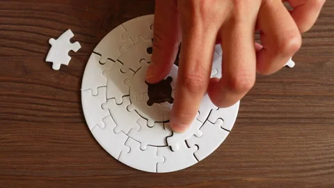 Hand Placing Puzzle Pieces into Circular Design on Wooden Table Stock Footage 295113152