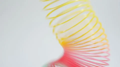 Hand placing a rainbow colored spring toy on a table sends it bouncing Stock Footage 283694867