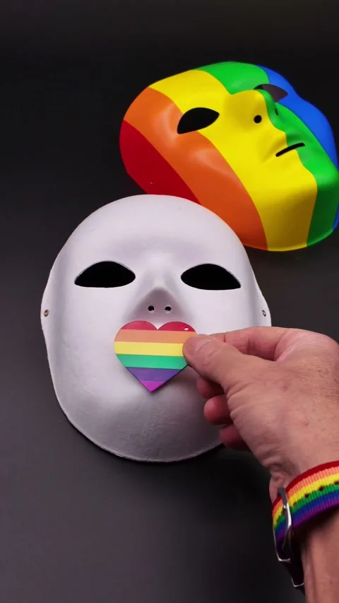 Hand placing a rainbow heart over the mouth of a white mask Video stock 329451734