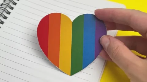 Hand placing a rainbow heart sticker in a notebook Stock Footage 336626994