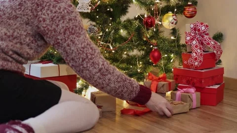 Hand placing red craft gift boxes under decorated Christmas tree blinking lights Stock Footage 164594926