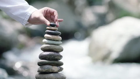 Hand placing a rock onto a balanced stack of rocks Stock Footage 336234304
