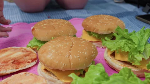 Hand Placing Sesame Bun on Delicious Homemade Cheeseburger Picnic Spread Stock Footage 342000248