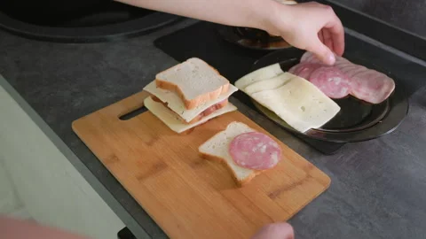 Hand placing slice of deli meat on sandwich stack with bread and cheese during Stock Footage 317927039