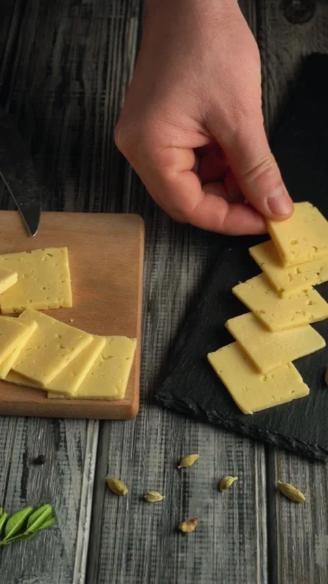 Hand placing sliced cheese onto a black slate board from a wooden cutting board, Stock Footage 337324029