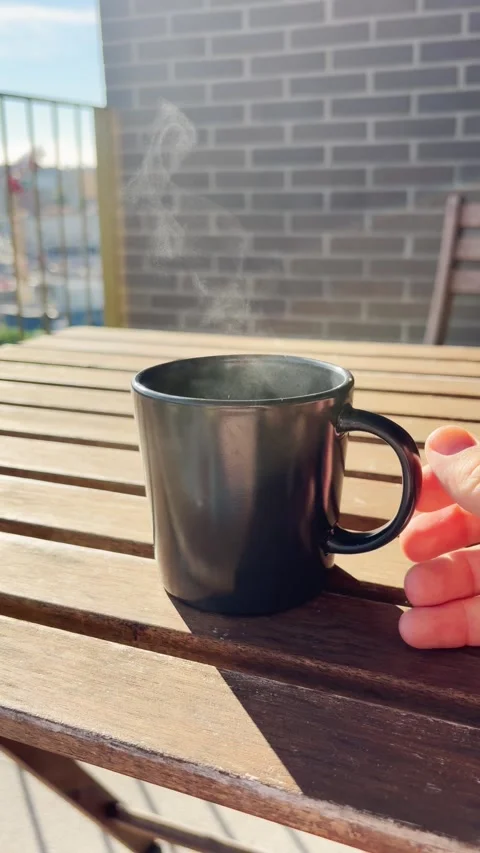 Hand placing a steaming cup of coffee on a wooden table outdoors Stock Footage 345694551
