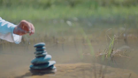 Hand placing a stone onto a balanced stack of rocks Stock Footage 336236309