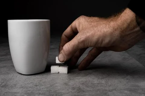 Hand Placing Sugar Cubes by White Mug Stock-Fotos