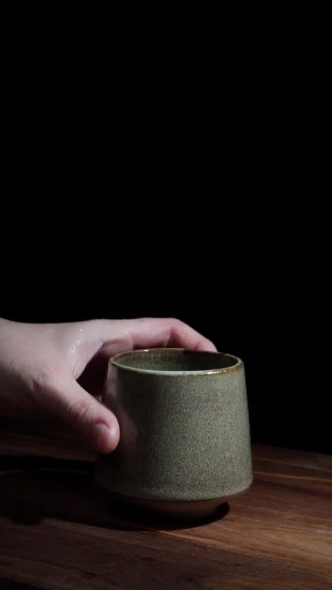 Hand placing textured ceramic cup on table dark background vertical Stock Footage 324761745