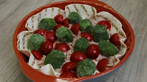 A hand placing tomatoes among spinach on meat, mozzarella and tortilla in a pan. Stock Footage 266421838
