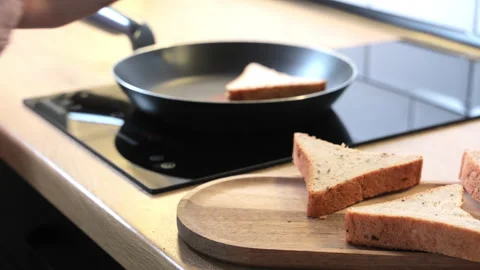 Hand placing triangular sandwich slices into a frying pan on a black induction 스톡 동영상 305587190