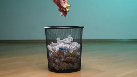 Hand placing a used yellow battery into a metal mesh trash can filled with Stock Footage 342759109