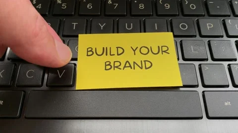 Hand placing yellow notepad with text build your brand on laptop keyboard Stock Footage 178745296