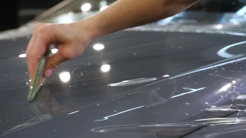 A hand with a plastic scraper glues a protective anti-gravel film on the new car Video stock 243810550
