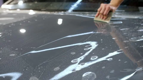 A hand with a plastic scraper glues a protective film on the new car hood. Video stock 246360983