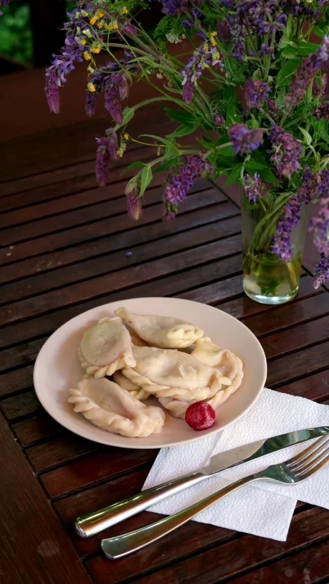 Hand plating red berries beside homemade varenyky dumplings on wooden table with Stock Footage 345161983