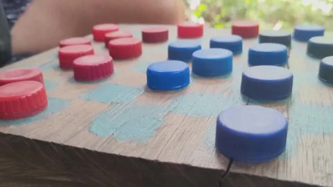 Hand playing a rustic game of checkers with recycled bottle caps. Stock Footage 312898219