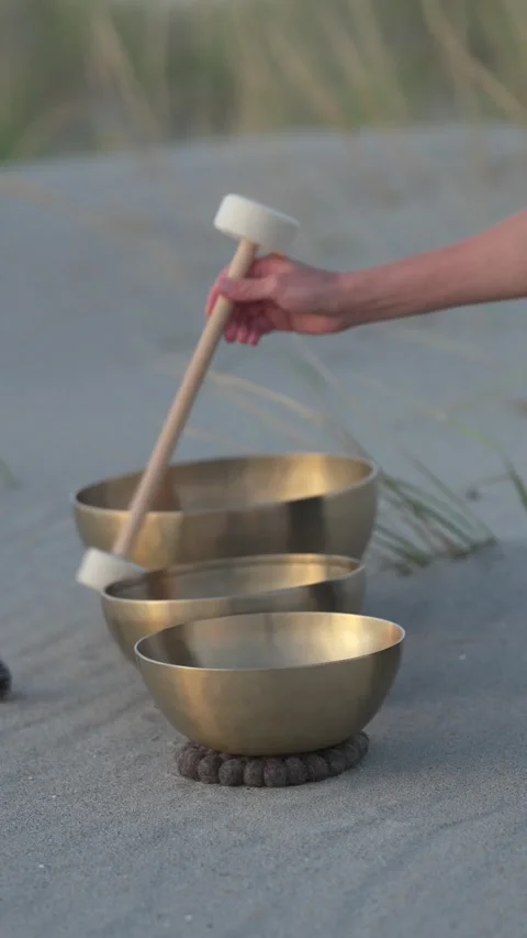 Hand playing singing bowls on a sandy beach at sunset Stock Footage 346504074