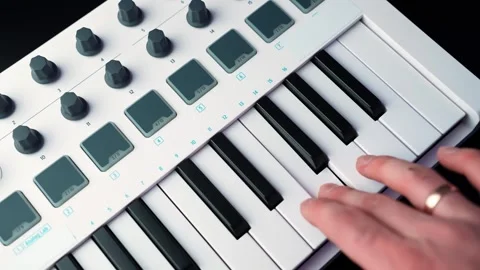 Hand plays a melody on a compact MIDI keyboard with pads and knobs, showing 库存影片 329600638