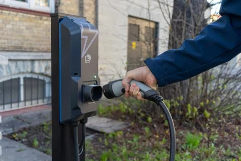Hand plugging cable into electric vehicle charging station outdoors Фото