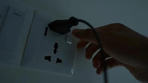 Hand plugging a device into a wall socket in dim lighting Stock Footage 317737275