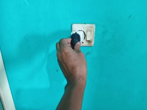 Hand plugging an electrical black cord into a wall socket Stock Photos
