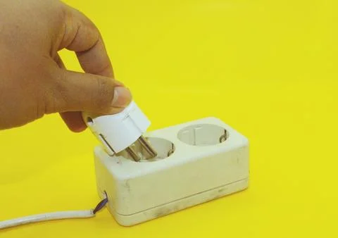 Hand plugging a power strip into a white socket on a yellow background Stock Photos