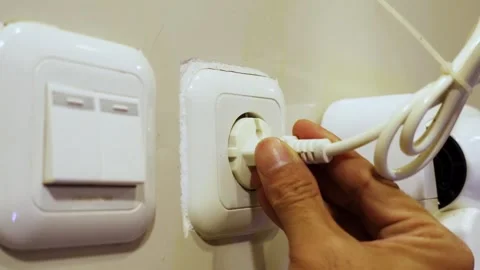 A hand plugging in socket to electrical outlet on wall Stock Footage 294696528