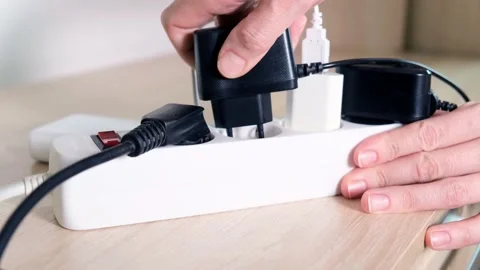 Hand plugging socket into electrical power strip overloaded with multiple Stock Footage 147685688