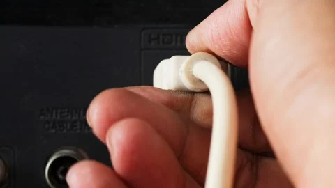 Hand plugging a white HDMI cable into an HDMI port on the back of a television. Stock Footage 344918055