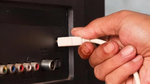 Hand plugging a white HDMI cable into an HDMI port on the back of a television. Stock Footage 344918061