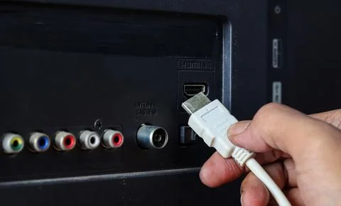 Hand plugging a white HDMI cable into an HDMI port on the back of a television. Stock Photos