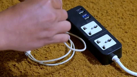 Hand plugging white power adapter into black power strip with USB-C cable Stock Footage 328522504