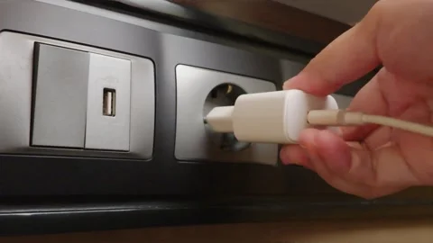 Hand plugging a white power adapter into an electrical wall socket to charge a d 動画素材 344092212