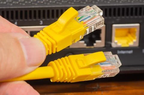 Hand plugging a yellow ethernet cable into a network router port, close-up. Stock Photos