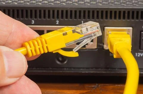 Hand plugging a yellow ethernet cable into a network router port, close-up. Stock Photos