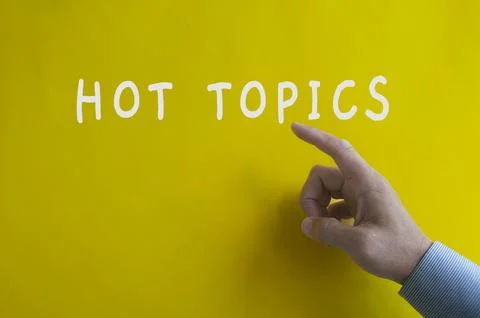 Hand pointing Hot Topics text on yellow cover background. Stock Photos