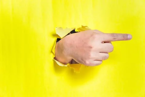A hand is pointing to the right side through a torn yellow paper, creating .. Foto stock