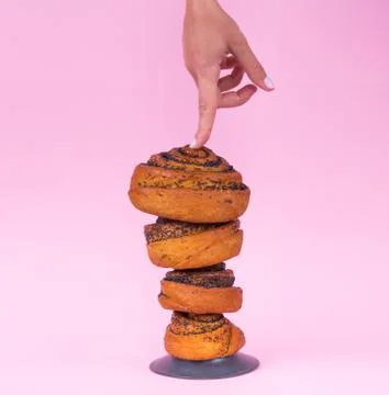 Hand points to a bun on a pink background. Baking advertisement. Stock Photos
