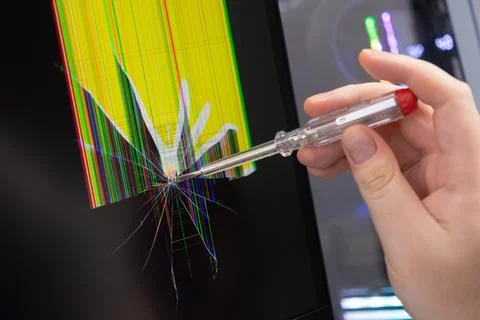 Hand points a clear screwdriver at a severely cracked computer screen displ.. Stock Photos