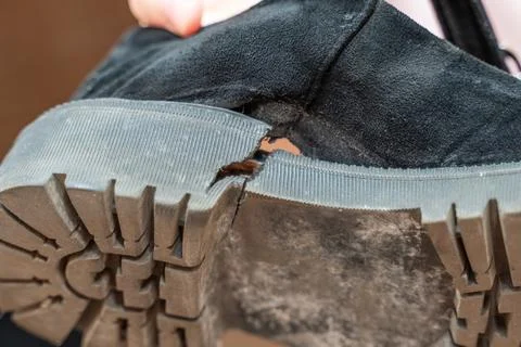Hand points through a hole in a worn-out shoe, highlighting the damage. The i Stock Photos