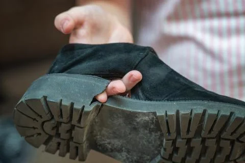 Hand points through a hole in a worn-out shoe, highlighting the damage. The i Stock Photos