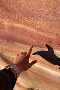 A hand points towards the natural patterns of colorful rock layers 스톡 사진