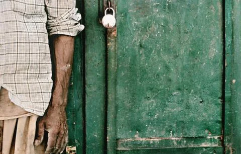 Hand of a poor old man infront of a green old wooden locked gate. Stock Photos
