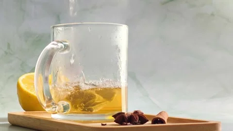 Hand pouring boiling water into clear glass cup over tea bag Stock Footage 336953536