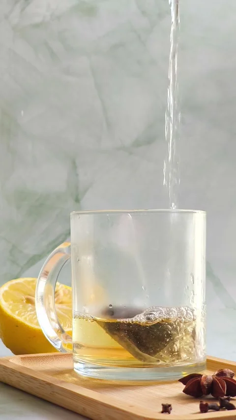 Hand pouring boiling water into clear glass cup over tea bag Video stock 336953674