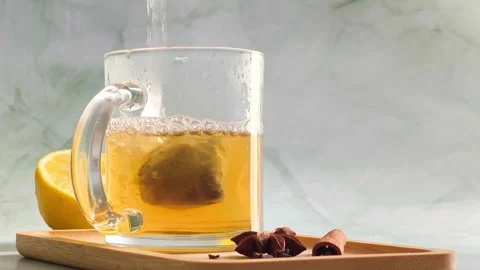 Hand pouring boiling water into clear glass cup over tea bag Stock Footage 336953773