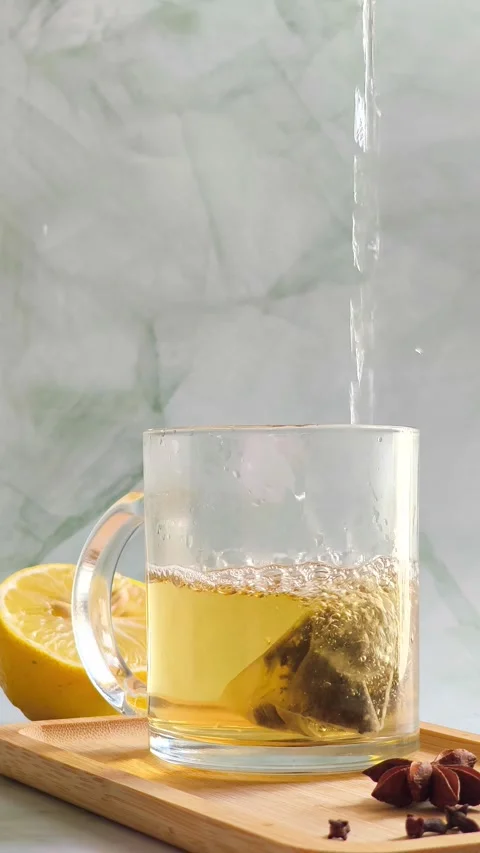 Hand pouring boiling water into clear glass cup over tea bag Stock Footage 336953817