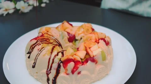 Hand Pouring Chocolate Syrup Over Fruit-Topped Dessert on Table Stock Footage 342874449
