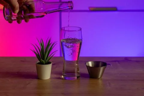 Hand pouring clear liquid into partially filled glass with plant and measuring Stock Photos